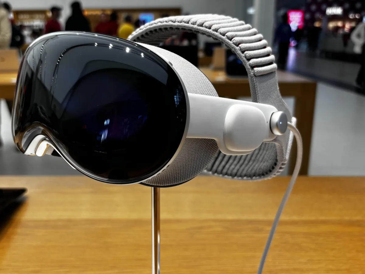An Apple Vision Pro headset with its grey knit band, on a display stand on a wooden table in a shop